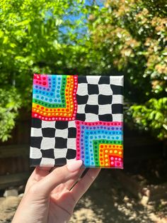 a hand holding up a small piece of art made out of colored squares and dots