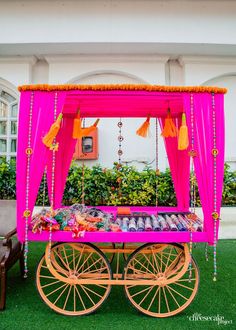 an elaborately decorated cart is sitting in the grass with pink drapes and tassels