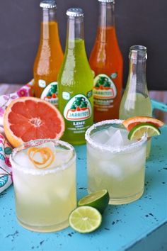 several different types of drinks on a table with limes and grapefruits