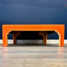 an orange table sitting on top of a hard wood floor next to a blue wall