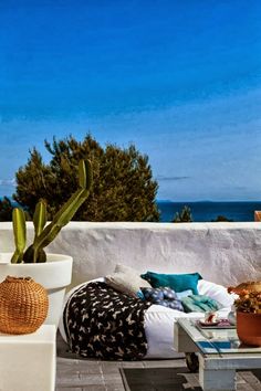 an outdoor patio area with potted plants and pillows on the floor, overlooking the ocean