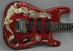 a red electric guitar with gold dragon decorations on it's body and neck, against a gray background