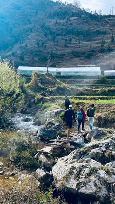 three people are walking on rocks near a stream