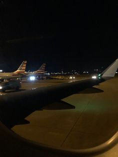 an airplane wing at night with the lights on and planes parked in the runway behind it