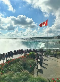 people are standing on the edge of a large waterfall with a canadian flag flying above it