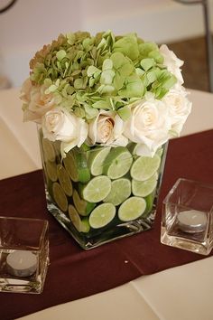 a vase filled with white flowers and green leaves on top of a table next to two glasses