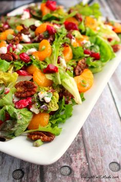 a white plate topped with a salad covered in oranges and other toppings on top of a wooden table