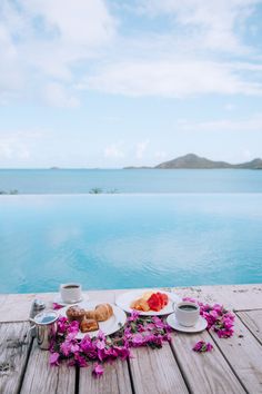 two plates with pastries and coffee on a wooden table near the water's edge