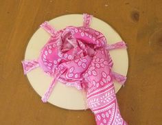 a white plate topped with a pink bandana on top of a wooden table next to a knife and fork