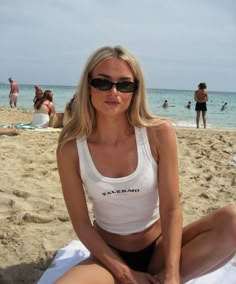 a woman sitting on top of a beach next to the ocean with people in the background