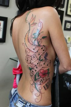 the back of a woman's body with music notes and flowers tattooed on it