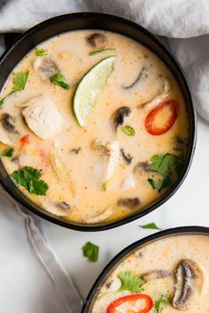 two black bowls filled with soup and garnished with cilantro, limes, tomatoes, and mushrooms