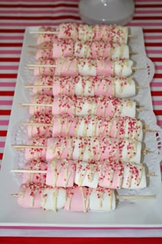 marshmallows and sprinkles are arranged on skewers on a plate