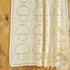 a white crocheted blanket on top of a wooden floor next to a plant