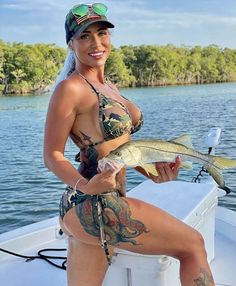 a woman in a bathing suit holding a fish on a boat with trees in the background