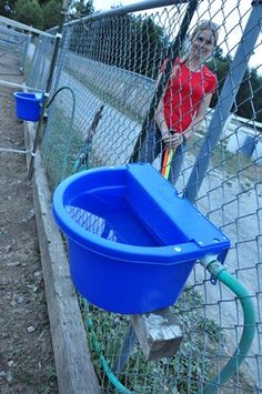 a woman standing next to a fence with a blue bucket and hose in front of it