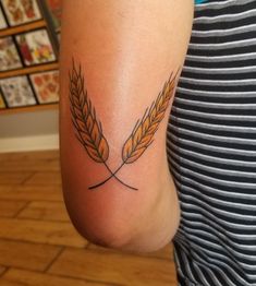 a person with a tattoo on their arm holding two wheat stalks in the shape of a twig