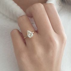 a woman's hand wearing a gold ring with a pear shaped diamond on it