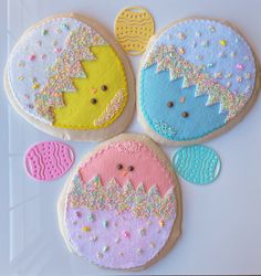 four decorated cookies with pastel colors and sprinkles are arranged on a white surface