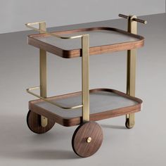 a wooden and metal serving cart with grey fabric on the bottom, gold handles and wheels