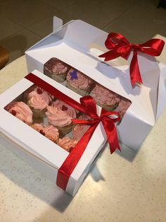 the cupcakes in the box are decorated with pink frosting and red ribbon