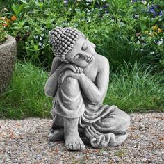 a buddha statue sitting on top of a gravel ground next to flowers and plants in the background