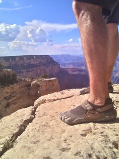 a man standing on the edge of a cliff with his feet in the air while wearing sandals