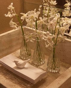 some white flowers are in vases on a bathroom counter top with a mirror behind them