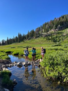 three hikers cross a stream in the mountains