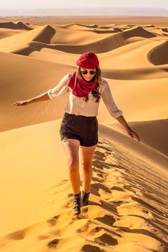 a woman walking across sand dunes in the desert