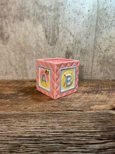 a pink origami block with letters on it sitting on top of a wooden table