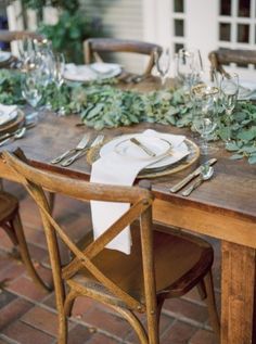 the table is set with place settings and greenery on it, along with silverware