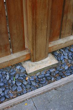 a cat sitting on the ground next to a wooden fence with rocks in front of it