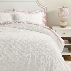 a white bed with pink flowers on it and two nightstands next to it in a bedroom