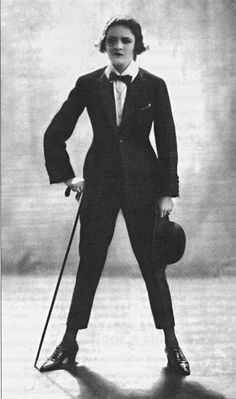 a woman in a suit and tie holding a cane with her hand on the hip