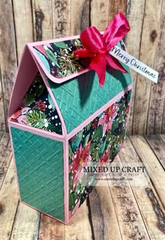 a green box with a red bow on the top and some pink ribbon around it