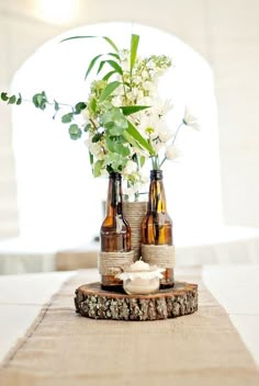 three beer bottles with flowers in them are sitting on a wooden slice that has been placed on a table