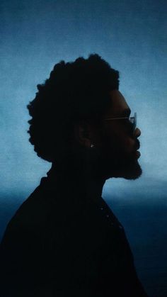 a man with dark hair and glasses standing in front of a blue background, looking off to the side