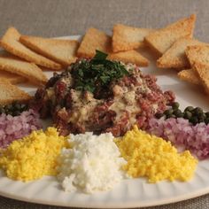 a white plate topped with different types of food next to crackers and bread wedges