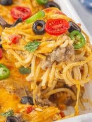 a casserole dish with pasta, olives, tomatoes and peppers on it