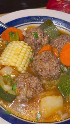 a blue and white bowl filled with meatballs, corn on the cob and carrots