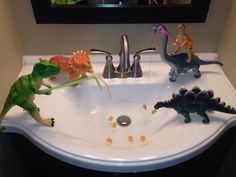 three toy dinosaurs playing in a bathroom sink