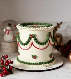 a white cake with green and red decorations on it sitting on top of a table