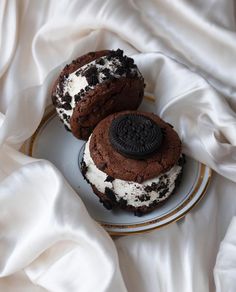 two cookies and oreo ice cream sandwiches are on a plate with white cloths