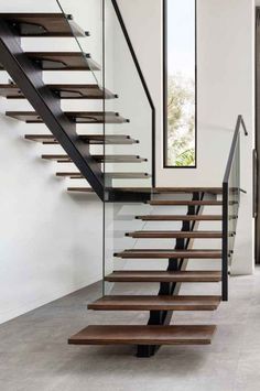 a modern staircase with glass railing and wooden handrails in an empty room next to a window