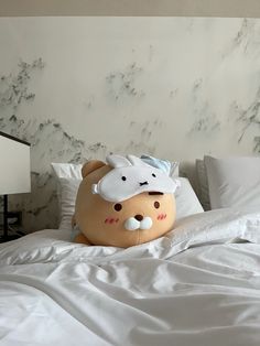 a large stuffed animal laying on top of a white bed covered in sheets and pillows