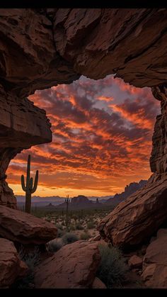 the sun is setting behind a large rock formation with a cactus in the foreground