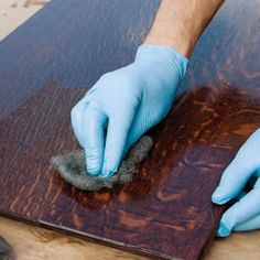 a person with blue gloves on polishing a piece of wood in preparation for painting