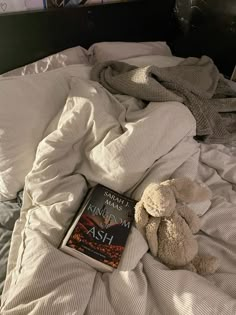 a teddy bear laying on top of a bed next to an open book and blanket