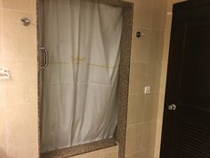 the shower curtain is open in this bathroom with beige tile walls and flooring, along with a black door